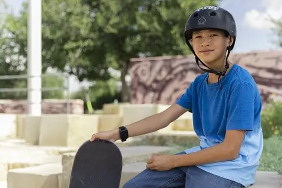 ​ tonårspojke med skateboard och hjälm bär vns therapy magnet på handleden